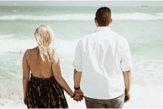 Photograph of a women and man holding hands looking out over the sea together.
