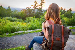 Photograph of a women sitting on a rock with a rucksack on her back looking over the woods.